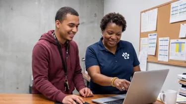 Two shelter staff members smiling at a laptop together behind the front desk