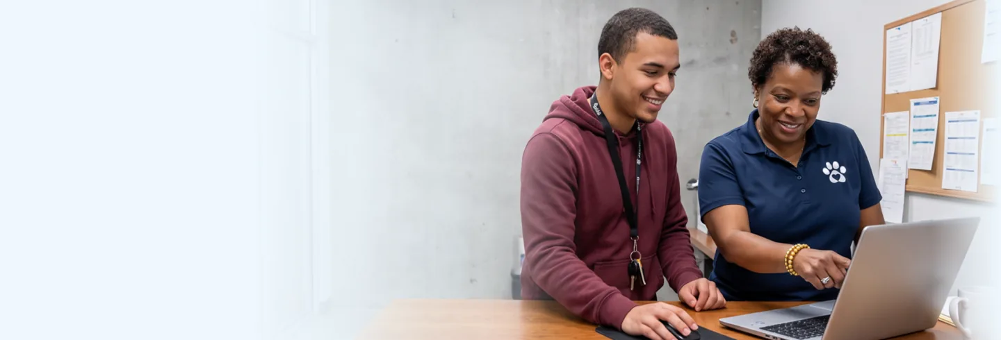 Two shelter staff members smiling at a laptop together behind the front desk